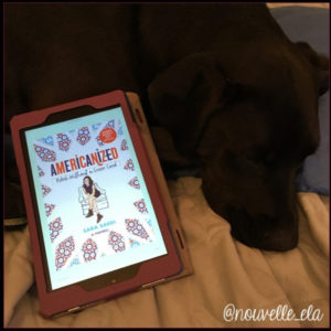 A dog lying down with a kindle beside it, displaying the cover of the book Americanized by Sara Saedi 