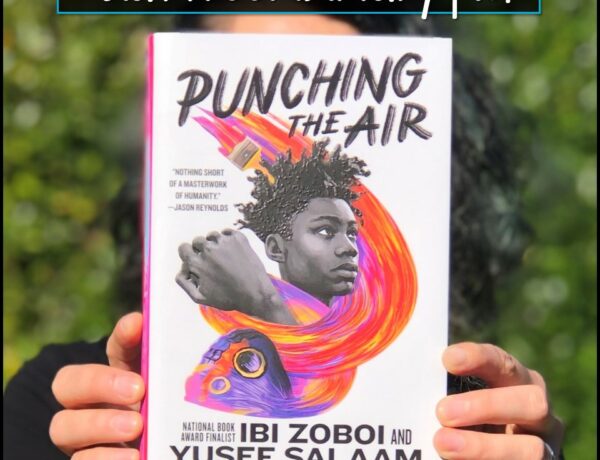 A photo of a woman holding up a copy of the book Punching the Air by Ibi Zboi and Yusef Salaam.