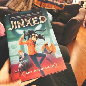 The book Jinxed by Amy McCullock help up in front of a living room