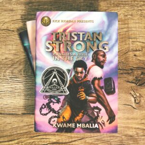 A woodgrain background and the book Tristan Strong Punches a Hole in the Sky by Kwame Mbalia